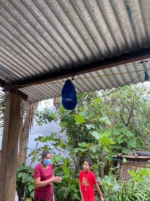 A University of Kentucky baseball hat hanging up, with people and plants in the background